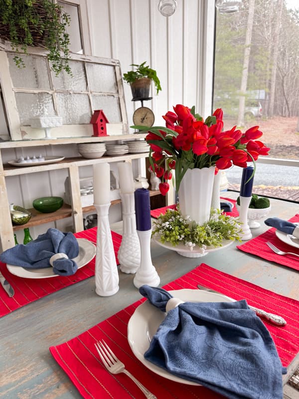 Red, white and blue table setting with  candleholder and red tulips in vase.  