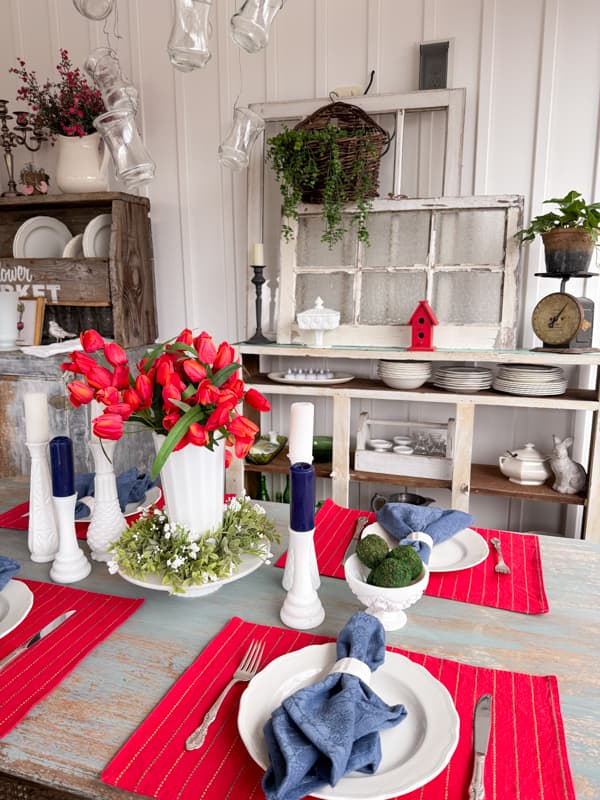 Red, white and blue table setting with vintage milk glass vase candleholder and red tulips in vase.