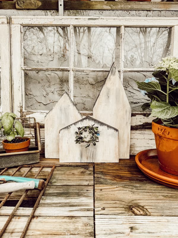 DIY wooden village with boxwood wreath on rustic potting bench for outdoor decor.  