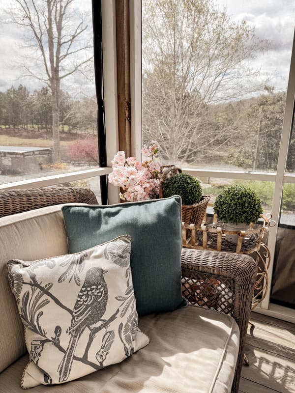 Blue bird pillow on screen porch with cherry blossom stems and boxwood topiaries for Spring Decorating.  
