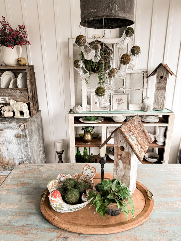 Centerpiece on farmhouse table with birdbath and DIY birdhouse with pot of ivy.