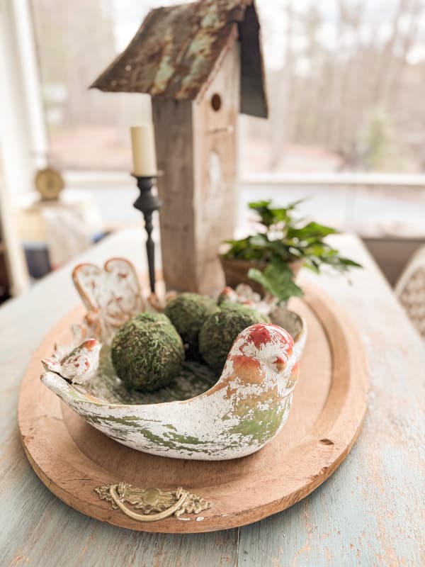 Centerpiece on farmhouse table with birdbath with pot of ivy. with decorative moss balls.  