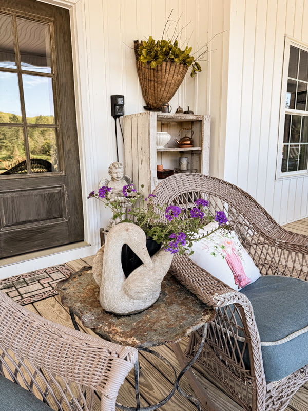Front porch sitting area with concrete swan and angel.  Vintage basket filled with greenery.  