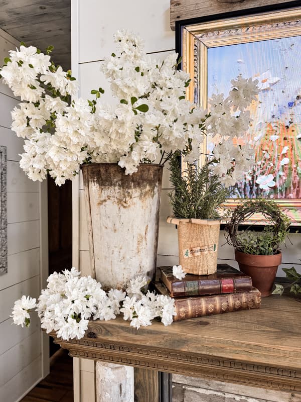 Vintage sap bucket filled with white azaleas and DIY old book page flower pot with fresh rosemary on vintage books