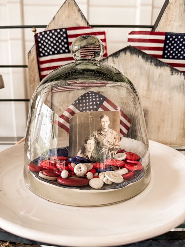 Vintage buttons with a military vintage photo under a glass cloche.  Patriotic american flags behind cloche.