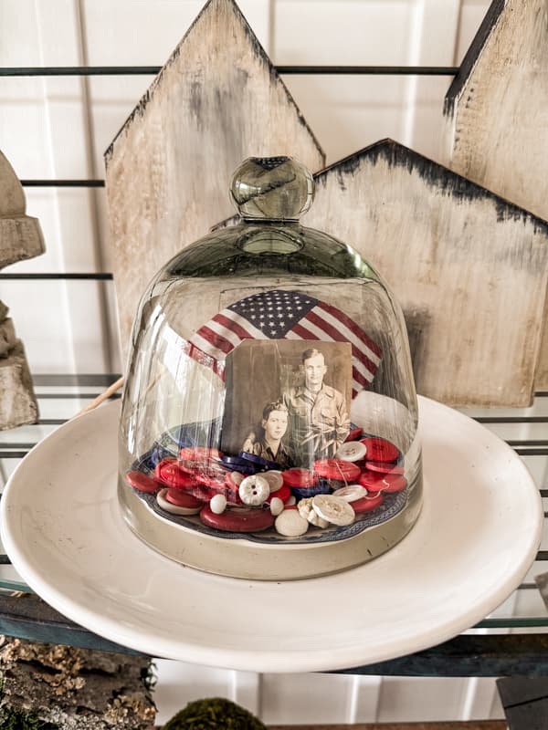 Vintage buttons with a military vintage photo under a glass cloche.  Patriotic american flags behind cloche.