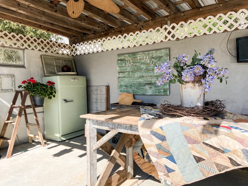 Outdoor Kitchen with old table and quilt in front of DIY Vintage Sign.