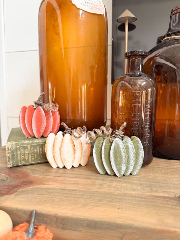 three wood pumpkins on mantel with amber bottles
