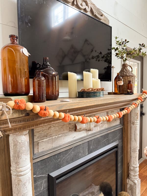 Fall Mantel with pumkin and wood bead garland, amber bottles and demijohn with leaf stems