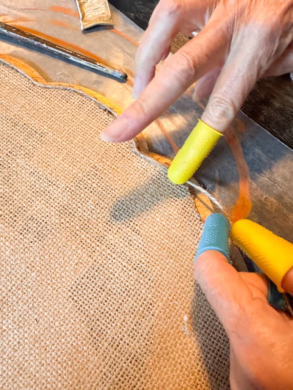 press jute twine into hot glue to cover the edge of burlap pumpkin