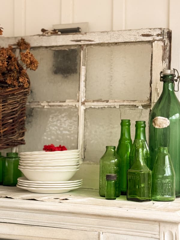 old window on top of china cabinet with green vintage bottles