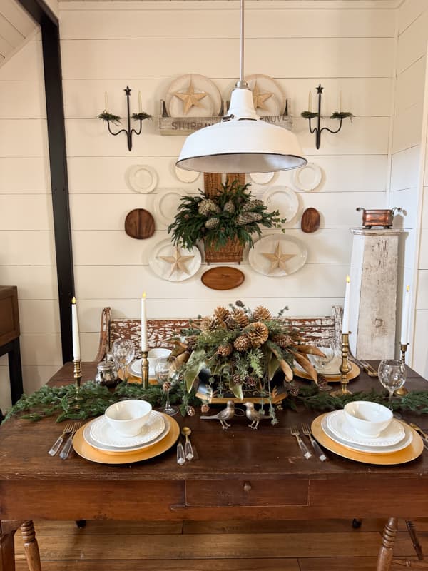 Dining room table setting for winter with white dishes, pinecones, and greenery
