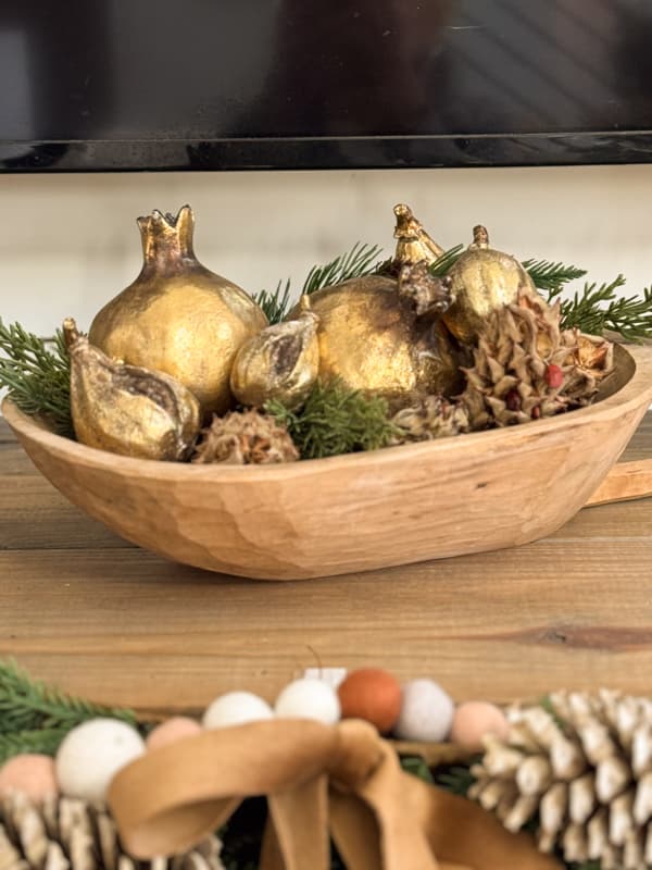 small dough bowl filled with gold fruit, greenery, and dried magnolia seed pods