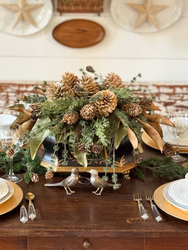 Table centerpiece with dried magnolia leaves, greenery and bleached pinecones with brass birds