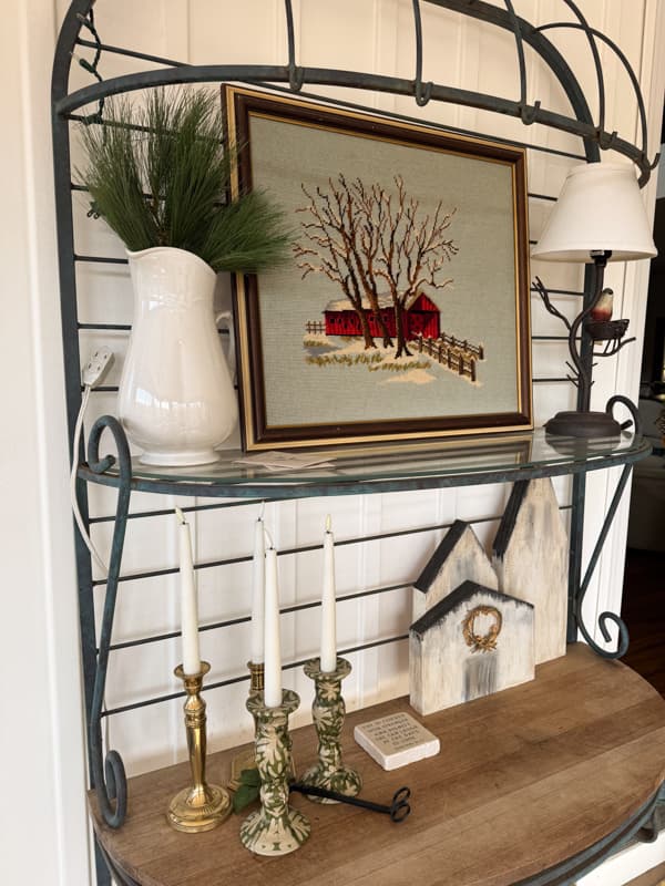 Bakers rack with vintage needlepoint covered bridge art and greenery