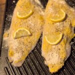 add lemon slices to mustard coat catfish on cast iron griddle ready for the oven