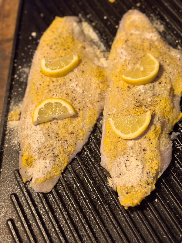 add lemon slices to mustard coat catfish on cast iron griddle ready for the oven