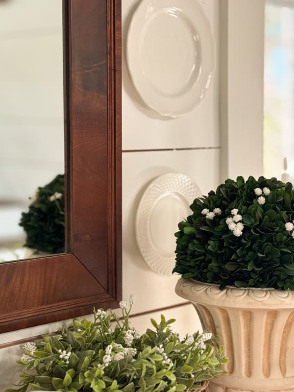 white plates on wall beside vintage mirror with boxwood plant