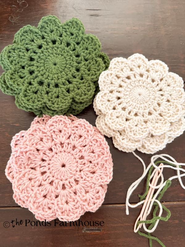 9 hand crocheted doilies in green, pink, and cream with needle & yarn.