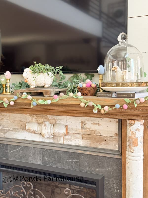 Easter mantel decorated with felt flower garland, lambs under a cloche 