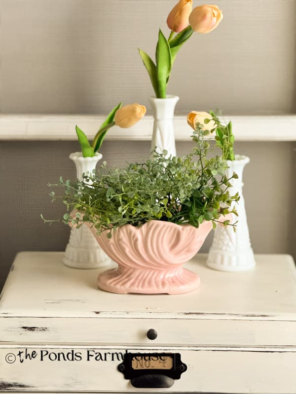 vintage pink planter with greenery and milk glass vases with tulips on bedroom side table.