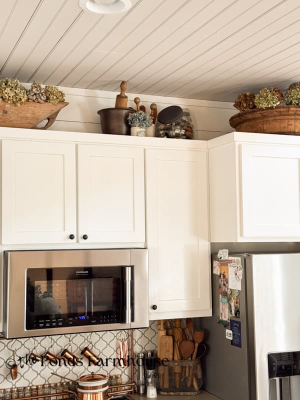 wooden dough bowl & gathering bowl with dried hydrangeas above kitchen cabinets