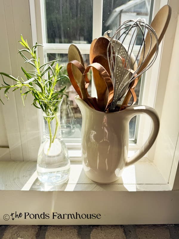 ironstone pitcher with vintage kitchen utensils and rosmary clipping in vase. on windowsill