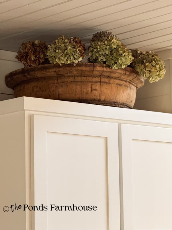 vintage European wooden bowl with dried hydreangas above kitchen cabinets
