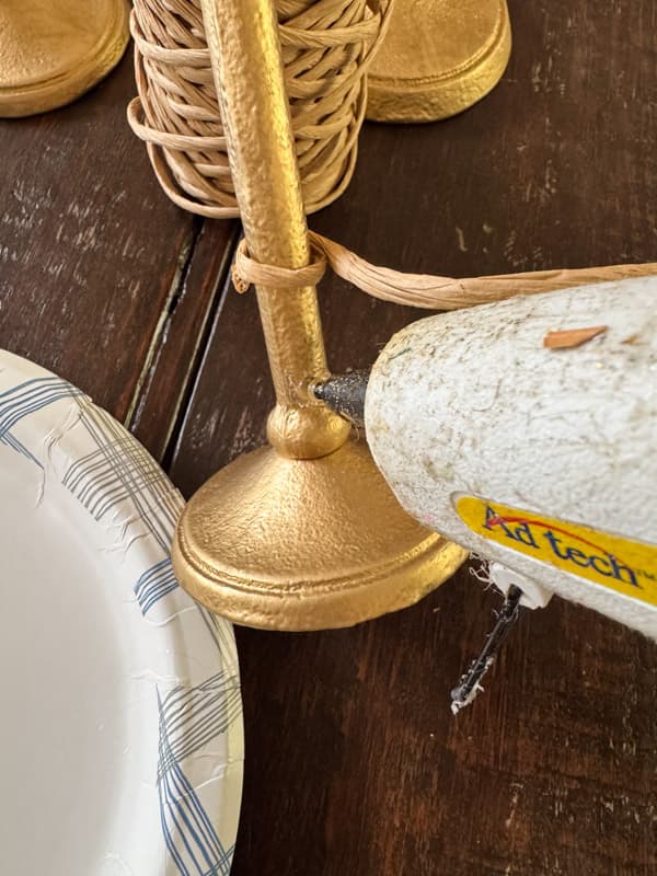 adding hot glue to attach raffia to base to create Serena & Lily Dupe Candlestick Holders
