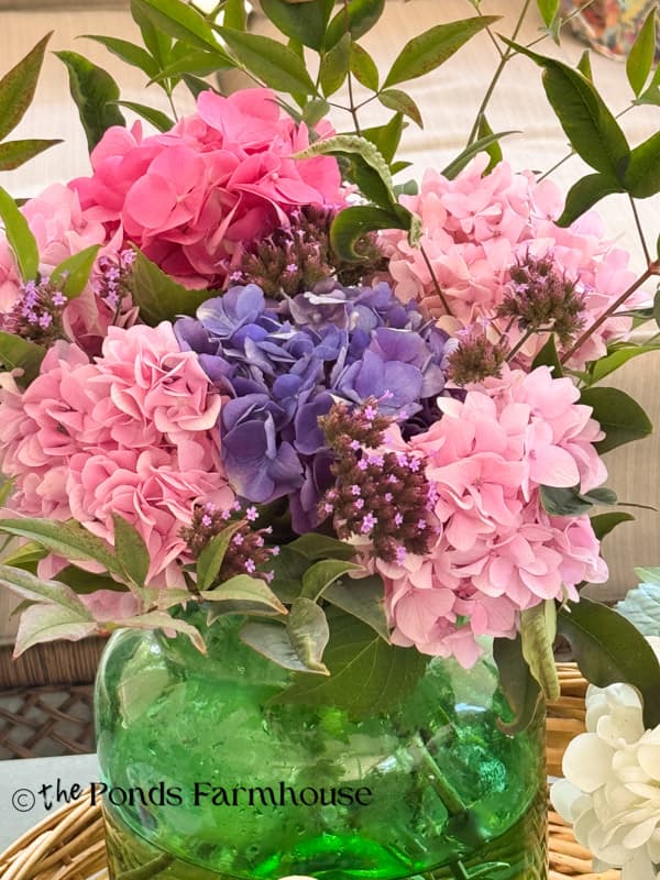 green glass canister filled with fresh hydrangea pink & blue blooms, lolly pop blooms and nanadina stems.