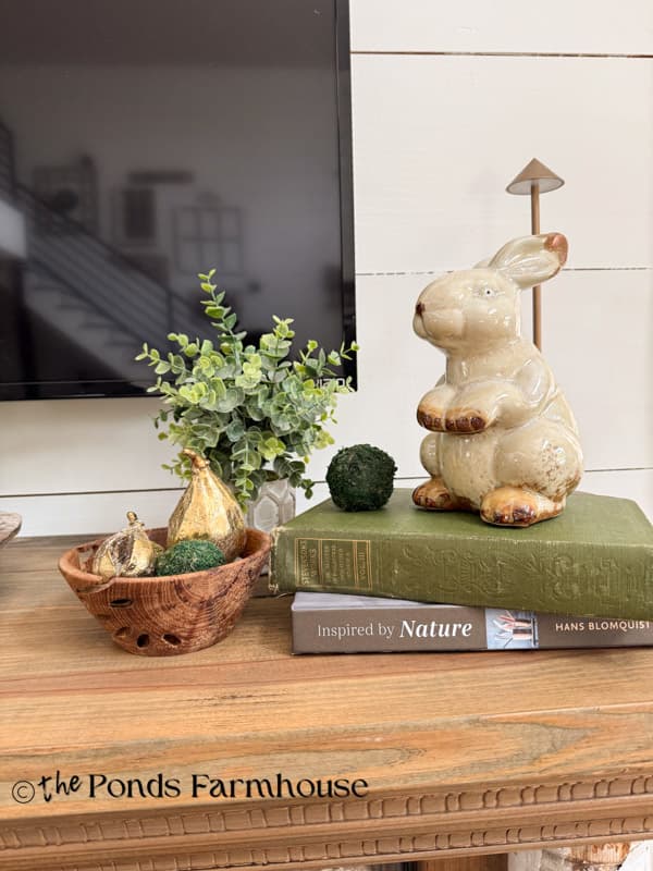 Moderately decorated Summer Mantel with vintage bunny, plant and wooden bowl of gold figs