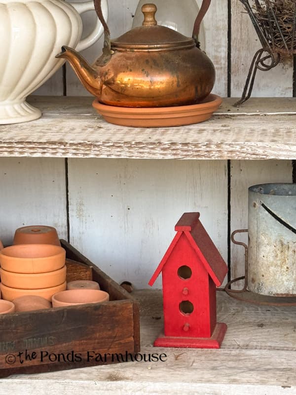small thrifted red birdhouse in primitive cabinet on front porch
