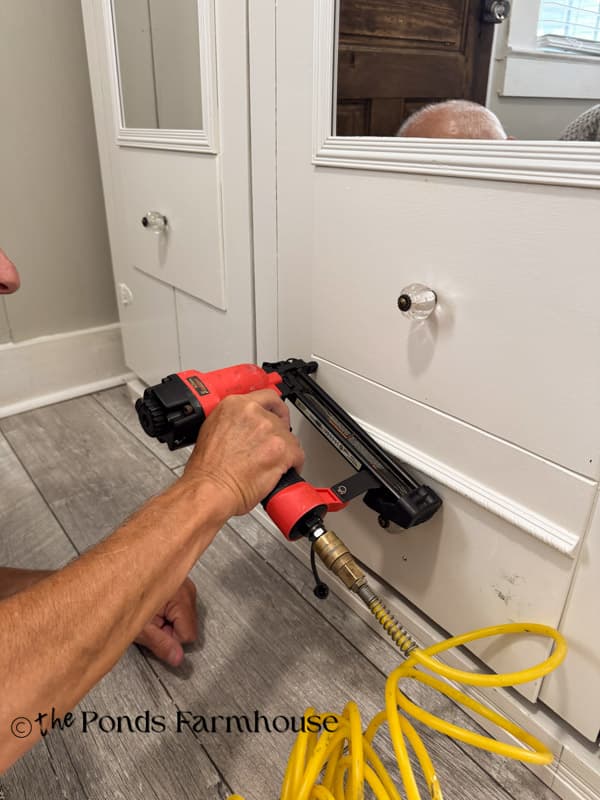 using a nail gun to attached the fake drawer fronts to the old wardrobe