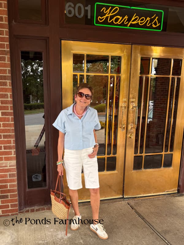 Rachel in white bermuda shorts and blue cropped button down. 