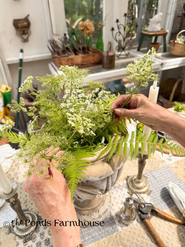 adding queen anne's lace stems to containers to create a wildflower centerpiece for summer garden party table