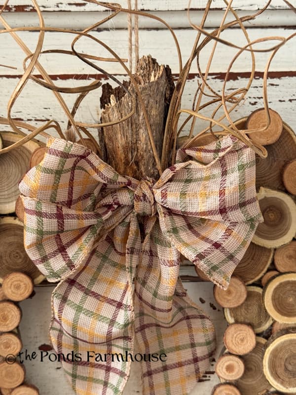 Close up of bow, wood stem and curly ting at top of pumpkin wreath