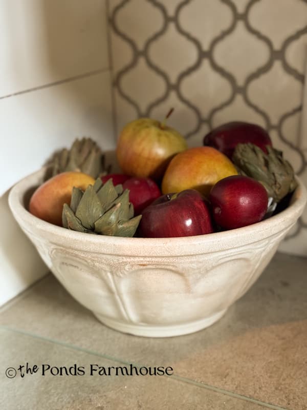 vintage bowl with apples and plums on kitchen countertop