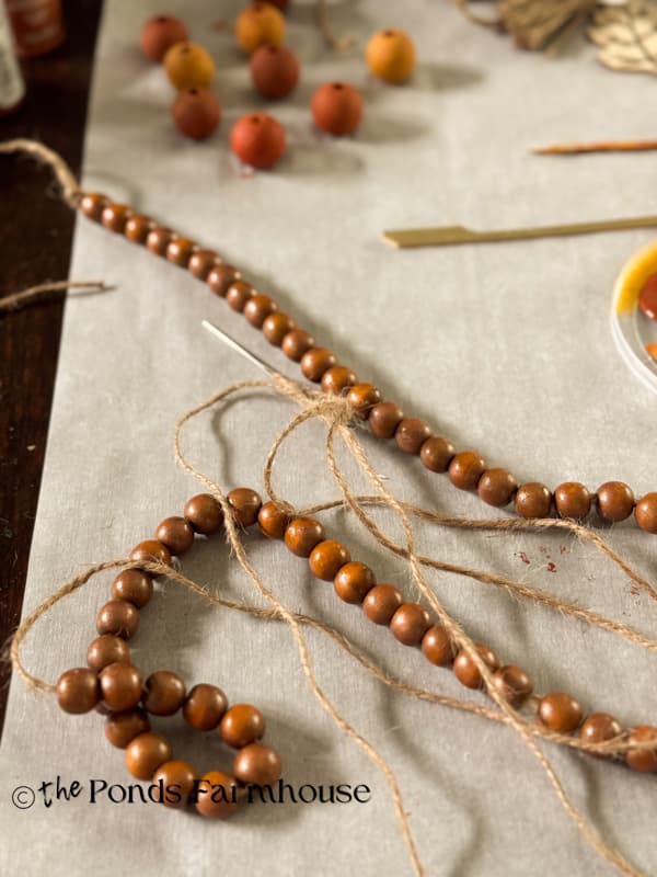 adding painted beads to jute twine with needle