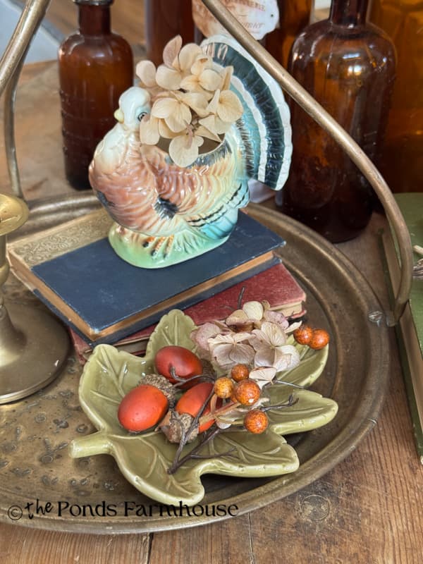 brass tray with turkey planters, old books, and leaf dish with acorns