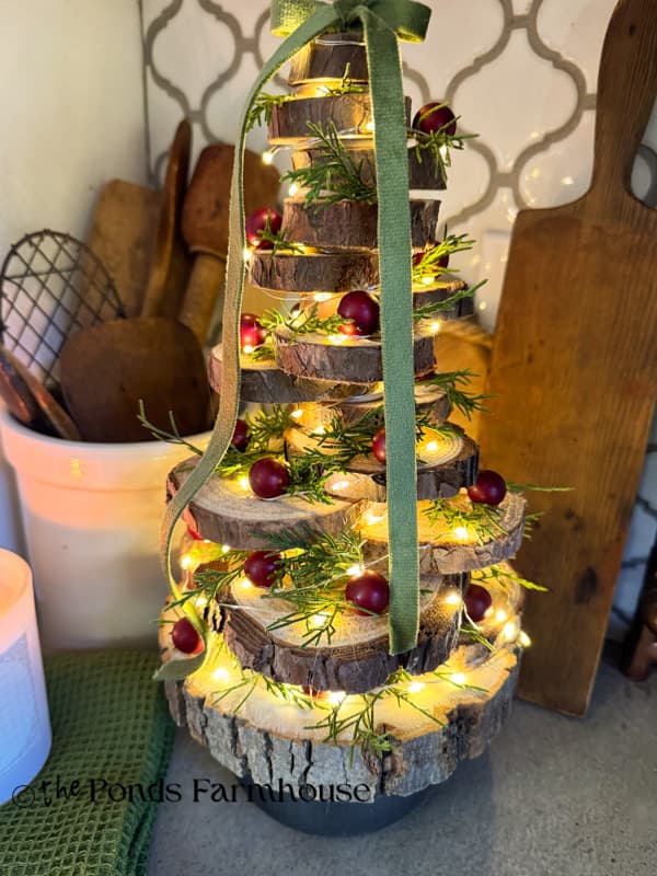 DIY Wood Slice Christmas Tree with berries, cedar, fairy lights and velvet Green bow on top to style kitchen countertops