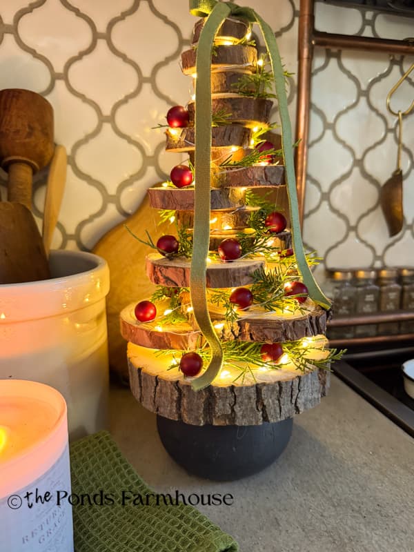 DIY Wood Slice Christmas Tree with berries, cedar sprigs, and fairy lights on kitchen countertop