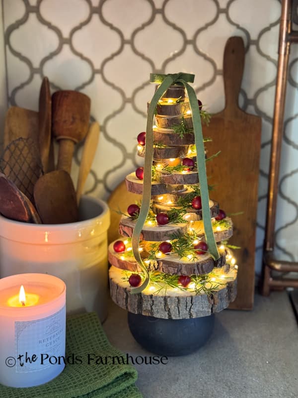 DIY Wood Slice Christmas Tree with berries, cedar, fairy lights, and bow at top on Kitchen countertop