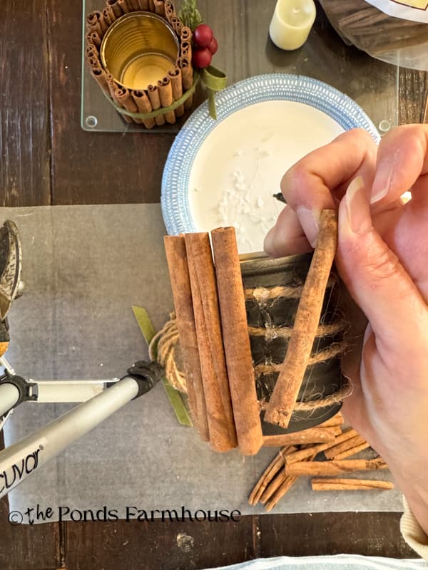 adding cinnamon stick to tin can with hot glue